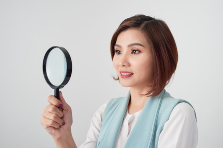 Close-up portrait of cheerful  woman in blue suite looking at camera through magnifying glass, isolated over white backgroundの写真素材