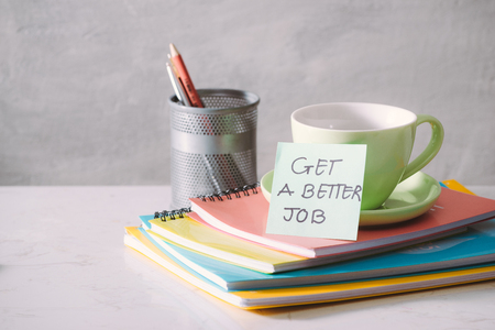 Green cup, notebooks and sticker with text - get a better job on light background. Toned business concept with copy spaceの写真素材