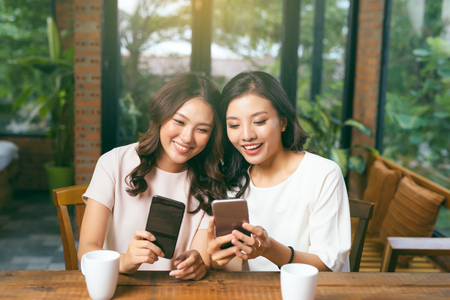 Two happy friends watching media content in a tablet sitting in a table at homeの写真素材
