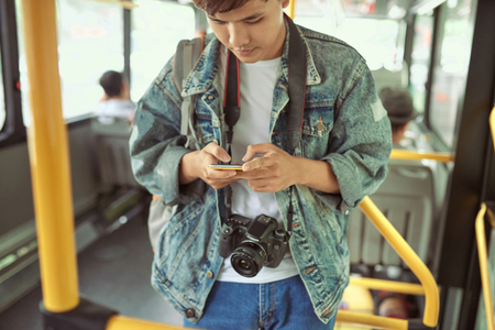handsome young man in a blue denim jacket using smartphone in busの写真素材