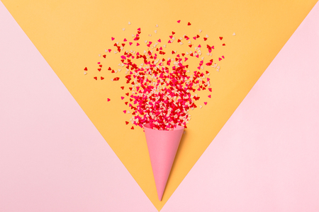 Paper cone and lot of small hearts on pink and yellow background. Romantic love background for Valentine's day, birthday, holiday, party, wedding. Flat lay.の写真素材