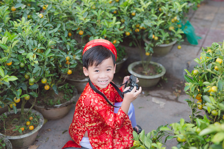 Child with digital compact camera outdoors. Cute little Vietnamese boy in ao dai dress smiling. Tet holidayの写真素材