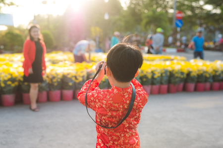 Little boy takes a photo of his mother on the digital camera at Tet flower marketの写真素材