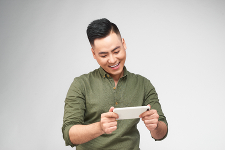 Excited bearded man in plaid shirt playing on smartphone over white backgroundの写真素材