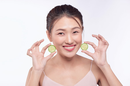 Young asian woman with cucumber slice in her hands isolated on white backgroundの写真素材