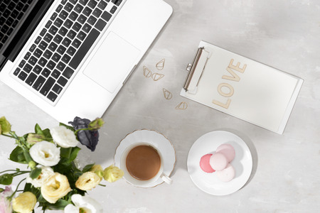 Feminine flat lay workspace with laptop, cup of tea, macarons, Love letter and flowers on white...