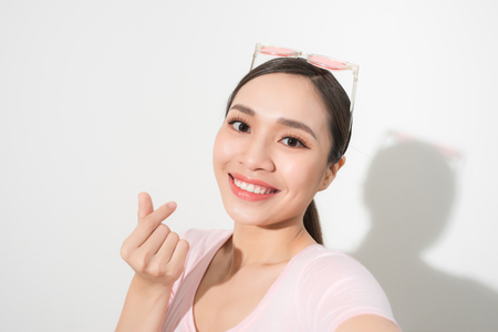 Studio portrait of beautiful woman smiling with white teeth and making selfie, photographing herself over white backgroundの写真素材