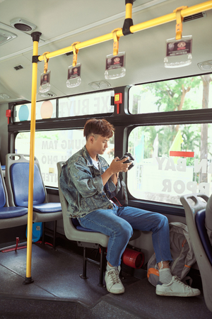 HO CHI MINH CITY, VIETNAM - 22 JULY, 2017: Young asian man taking a photo on bus with her digital cameraの写真素材