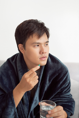 Handsome young man with pill and glass of water at homeの写真素材