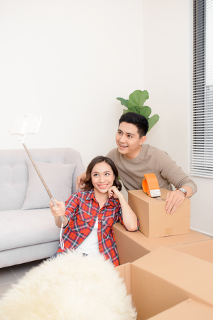 home, people, repair and real estate concept - smiling couple with big cardboard boxes moving to new place and taking smartphone selfieの写真素材