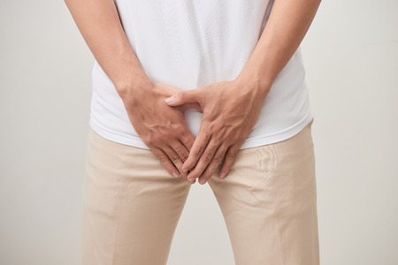Man hands holding on middle crotch of trousers with pain action isolated on white background.