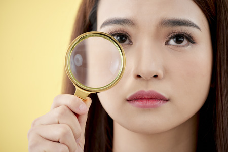 Woman with magnifying glass isolated on a yellow backgroundの写真素材