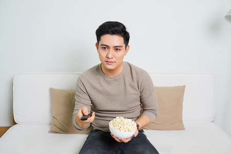 Bored man watching tv and zapping sitting on a couch at homeの写真素材