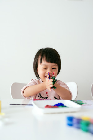 Little asian girl painting with paintbrush and colorful paintsの写真素材