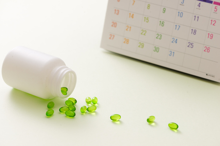 Medical pills capsule in pill box with calendar on white background.の写真素材