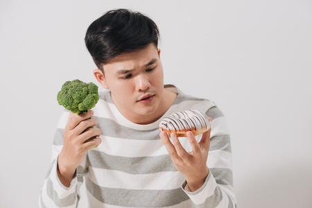 Man having hard choice between healthy and unhealthy foodの写真素材