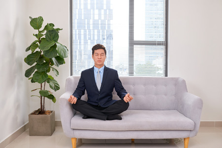 A young businessman meditating on sofa in officeの写真素材