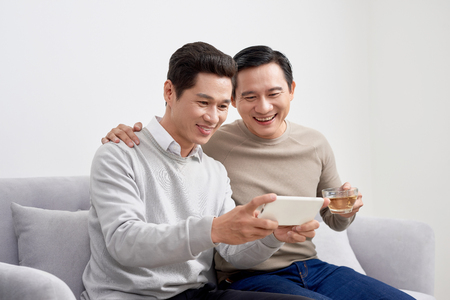 Cheerful young men dressed in casual wear smiling at camera while making selfie photo on front cameraの写真素材