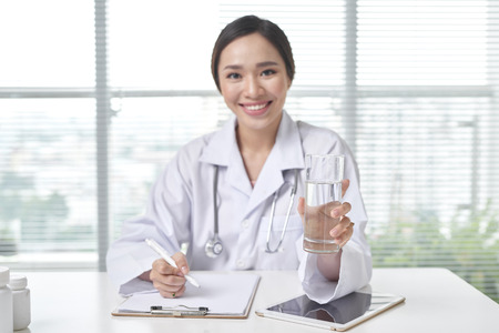 Smiling Female Doctor offering a glass of water in her Officeの写真素材