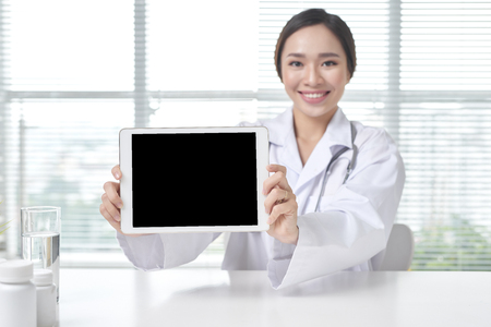 female doctor showing tablet with blank screen to patient at officeの写真素材
