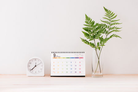 Mockup with a calendar with a white center against the background of a white wall with a alarm clock, leaves in vaseの写真素材