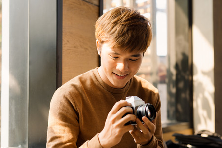 Cropped view of male amateur dressed in yellow sweater making setting on display of vintage camera...
