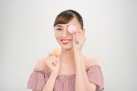 Portrait of a beautiful young woman wearing pink dress standing isolated over pink background, holding macaroonsの写真素材