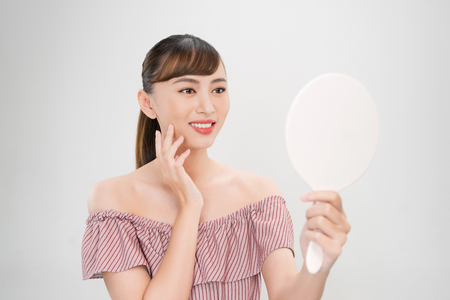 Pretty asian woman with clear skin looking at the mirrorの写真素材