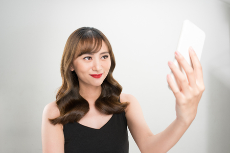 Smiling young girl making selfie photo on smartphone over gray backgroundの写真素材
