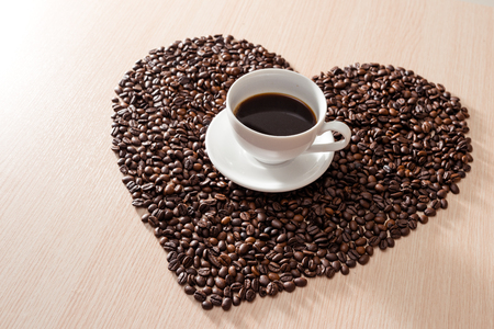 Coffee cup in the middle of shape love coffee beans on the wooden backgroundの写真素材