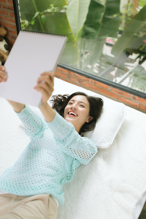 Beautiful young asian woman laying on bed and writing a diary.の写真素材
