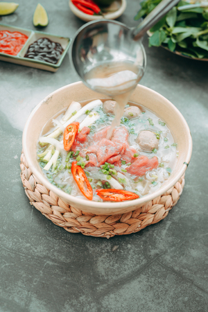 Pho Bo - Vietnamese fresh rice noodle soup with beef, herbs and chili. Stock being poured. Vietnam's national dish.の写真素材