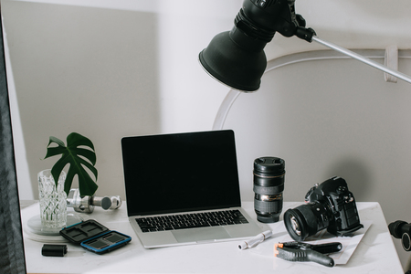 Still life working from home desk with professional photographic equipment, camera, lens, computer monitor, electronics indoors.の写真素材