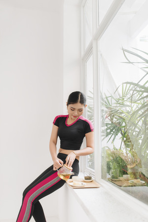 Happy young asian woman tea near window in the morningの写真素材