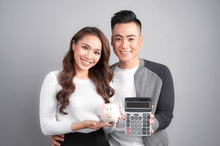 young couple hold pink pig bank and calculator isolated on gray backgroundの写真素材