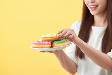Beautiful young woman smiling holding a plate full of delicious color donutsの写真素材