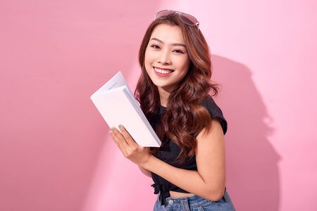 Image of smiling young woman posing isolated over pink background wall holding book reading.の写真素材