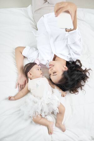 Young mother and cute baby on bed at homeの写真素材