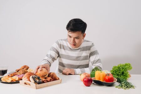 healthy lifestyle concept - smiling young man comparing healthy and unhealthy food. fresh vegetables and hamburger.の写真素材