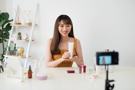 Young female blogger with makeup cosmetics recording video at homeの写真素材