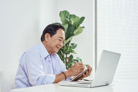 Senior man at home connected on laptop computerの写真素材