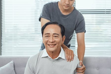 Asian old man shoulder pain, sitting on sofa , son massaging father shoulder.の写真素材