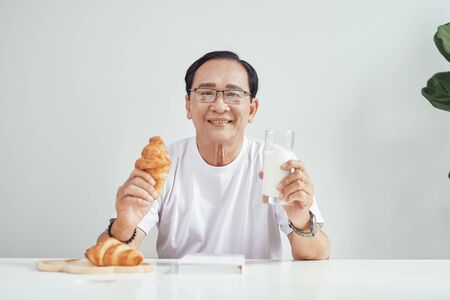Breakfast at morning. Elder person holding croissant with glass of milk. Healthy food.の写真素材