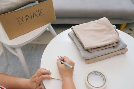 Volunteer writing in notebook and near carton box with clothes