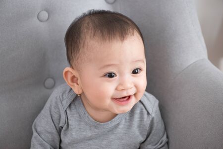 Closeup portrait of cute adorable smiling laughing, baby girl with black eyes sitting on sofa looking away from camera, natural window light, lifestyleの写真素材