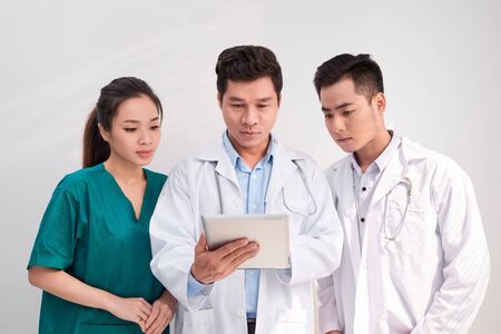 Medical team includes doctors and nurse looking at an ipad/tablet computer togetherの写真素材