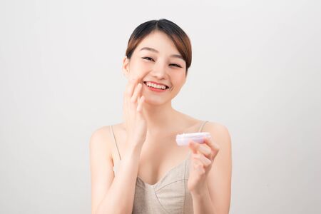 Cheerful young woman applying face cream isolated on whiteの写真素材