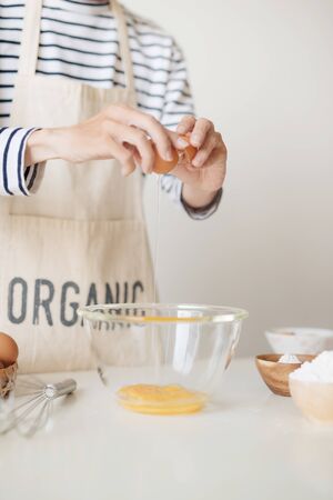 Horizontal shot of serious male wearing beige apron breaking egg into metal bowl