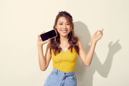 Portrait of a cheerful beautiful girl showing or presenting mobile phone application and pointing...