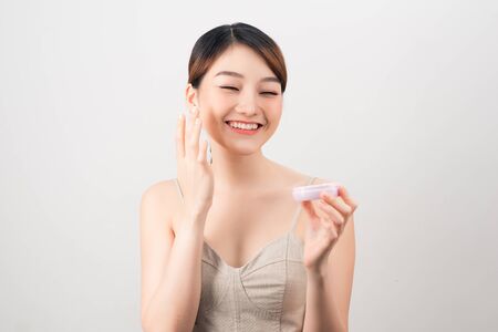 Cheerful young woman applying face cream isolated on white backgroundの写真素材
